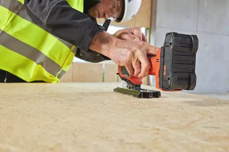 A worker with a cordless jig saw SJT 6-22 and a B22-55 battery cuts an OSB plate.