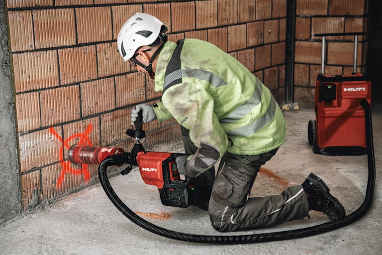 Persona arrodillada perforando pared con herramienta Hilti