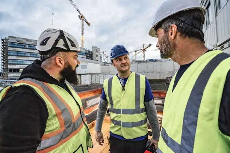Three male workers in conversation on jobsite, carrying Hilti cases