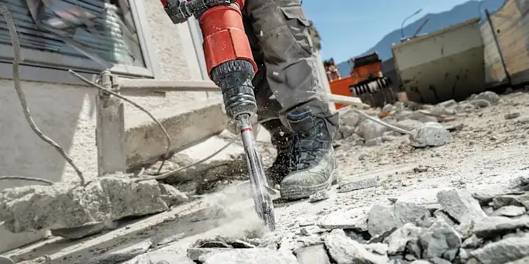 Hilti Meißelhammer mit Flachspitzmeißel beim Aufbrechen von Beton, umgeben von Bauschutt auf einer Baustelle.