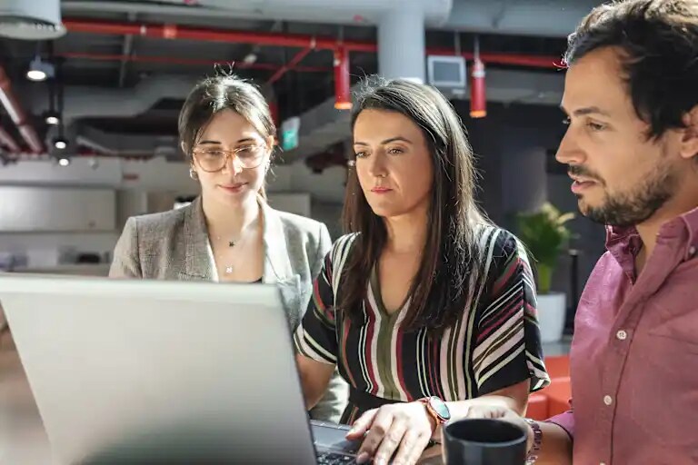 Due dipendenti donne e un dipendente uomo riuniti davanti a un computer in un ufficio di Dubai.