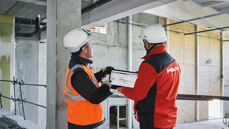 Un gestionnaire de compte Hilti présente la version tablette du logiciel ERP 4PS (capture d'écran) à un professionnel du BTP sur un chantier de construction.