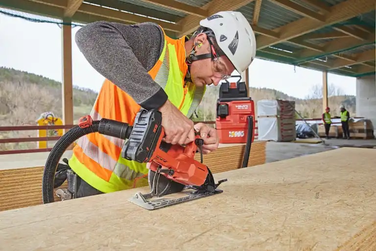 Worker is cutting an OSB plate with a circular saw SC 6WL-22. The circular saw is connected to a cordless vaccuum cleaner VC 10-22 with remote control