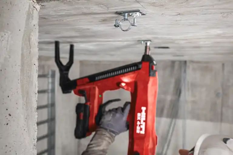 Construction worker doing a roof overhead application using the BX 4-22 with the B22-85 battery to install the BX threaded element with a mounted cable conduit clamp