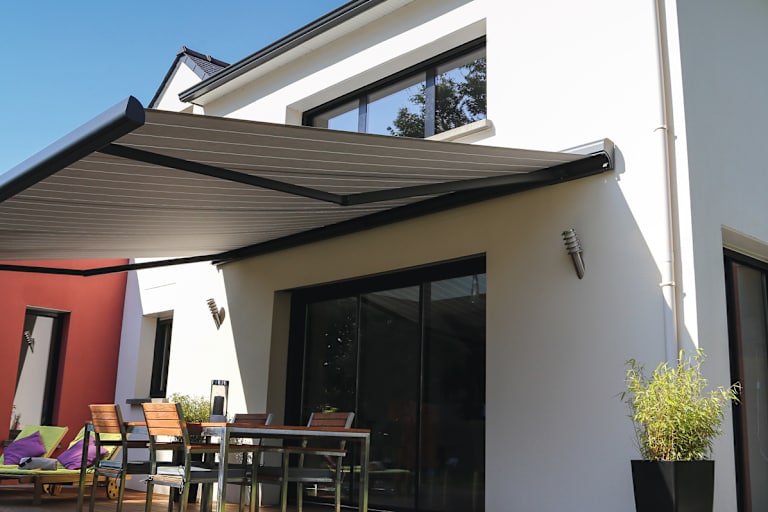 Afbeelding van een modern terras bij een woning, beschermd door een aan de gevel gemonteerde uitschuifbare zonwering.