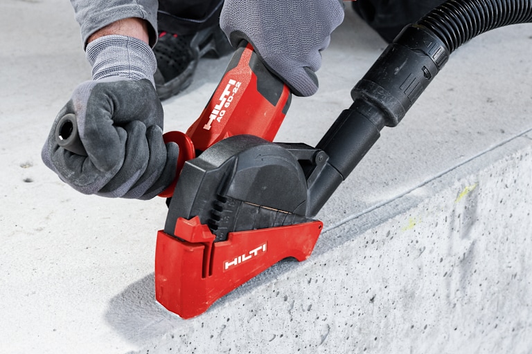 Persoon gebruikt een Hilti-haakse slijper om beton te snijden, met een aangesloten stofafzuigslang