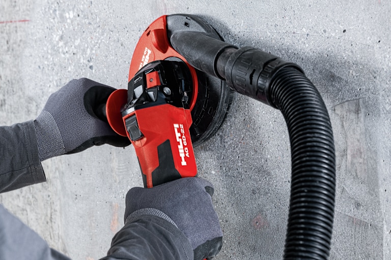 Persoon gebruikt een Hilti-haakse slijper om beton te slijpen, met een aangesloten stofafzuigslang