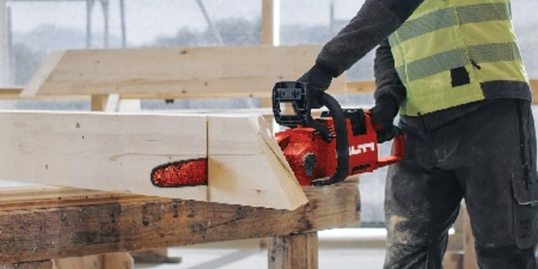 Un ouvrier coupe un morceau de bois avec une tronçonneuse sans fil