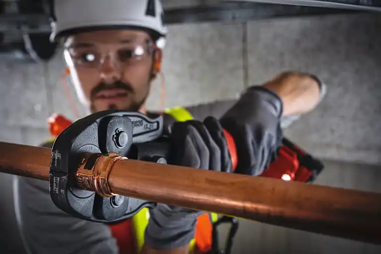 Construction worker using the NPR pipe press tool with hydraulic jaws to connect overhead pipes