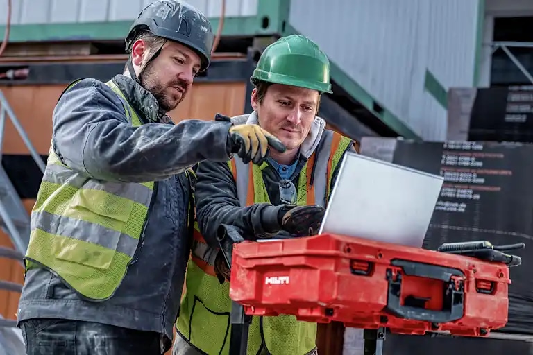Twee arbeiders die naar het scherm van een laptop wijzen die boven op een ProKit staat