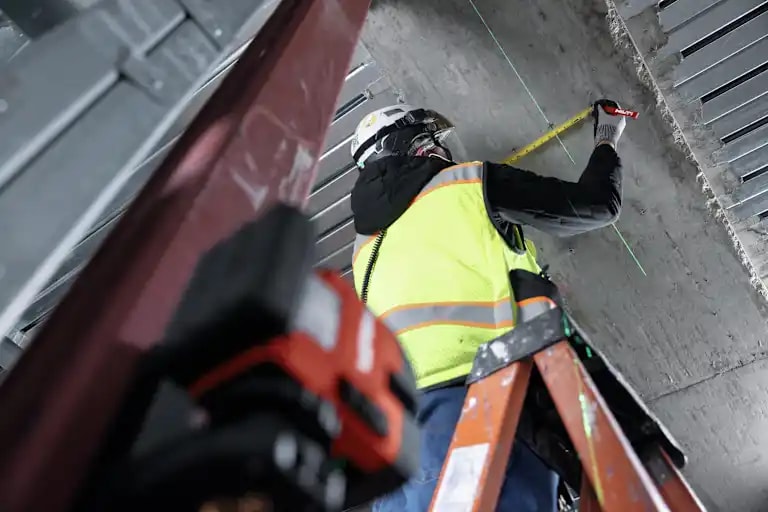 Application Image - Worker standing on ladder - KH-EZ IQ push-to-connect screw anchor + PM 20-CG Plumb and Cross Line Laser