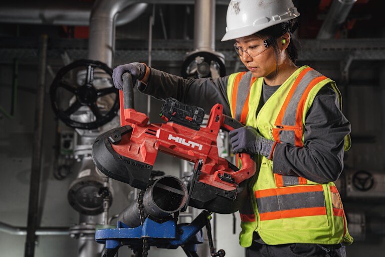 Een werkneemster gebruikt een bandzaag met diepe snede SB 6-22 om een dikke metalen buis te snijden