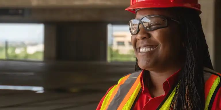 A female jobsite worker is wearing the security helmet and PPE glasses while smiling