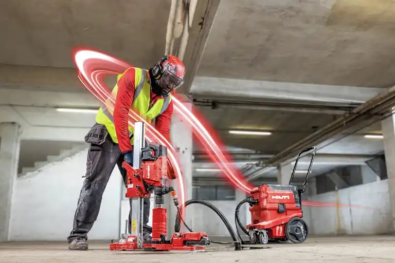 Application image of a worker using a DD 160‑22 Cordless Core Drill with dust extraction to drill a core hole in concrete during indoor construction work.