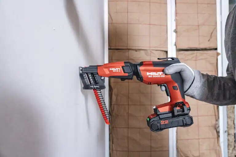 Client fixant une plaque de plâtre sur des rails à l’aide de la visseuse plaquiste SD 5000-22 équipée du chargeur de vis SD-M 2.