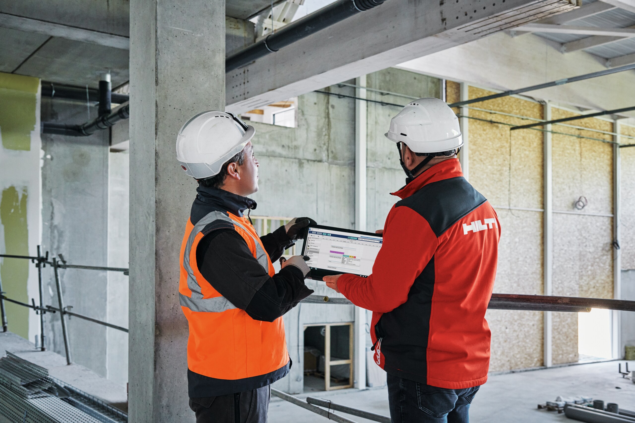 Un gestionnaire de compte Hilti présente la version tablette du logiciel ERP 4PS (capture d'écran) à un professionnel du BTP sur un chantier de construction.