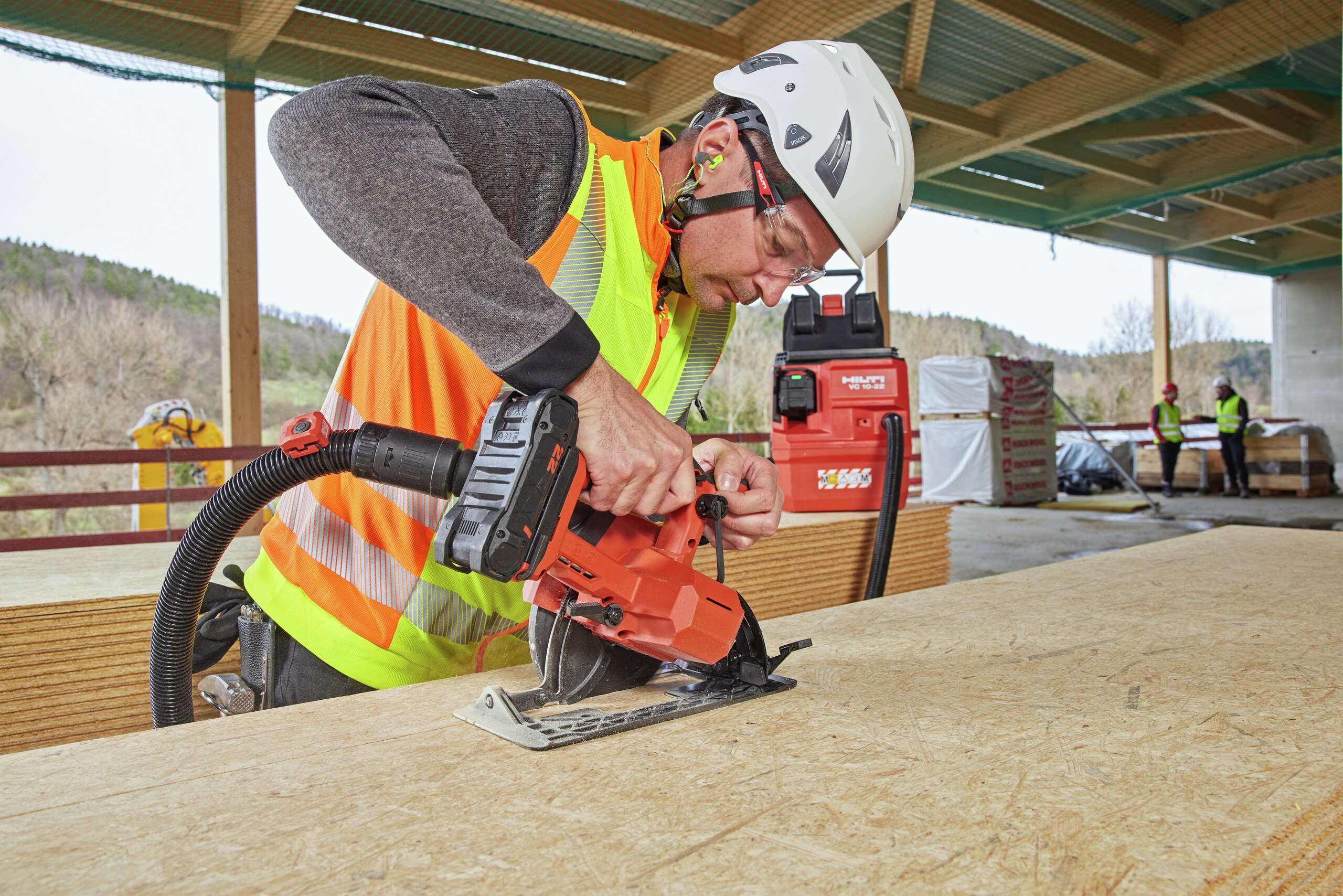 Worker is cutting an OSB plate with a circular saw SC 6WL-22. The circular saw is connected to a cordless vaccuum cleaner VC 10-22 with remote control