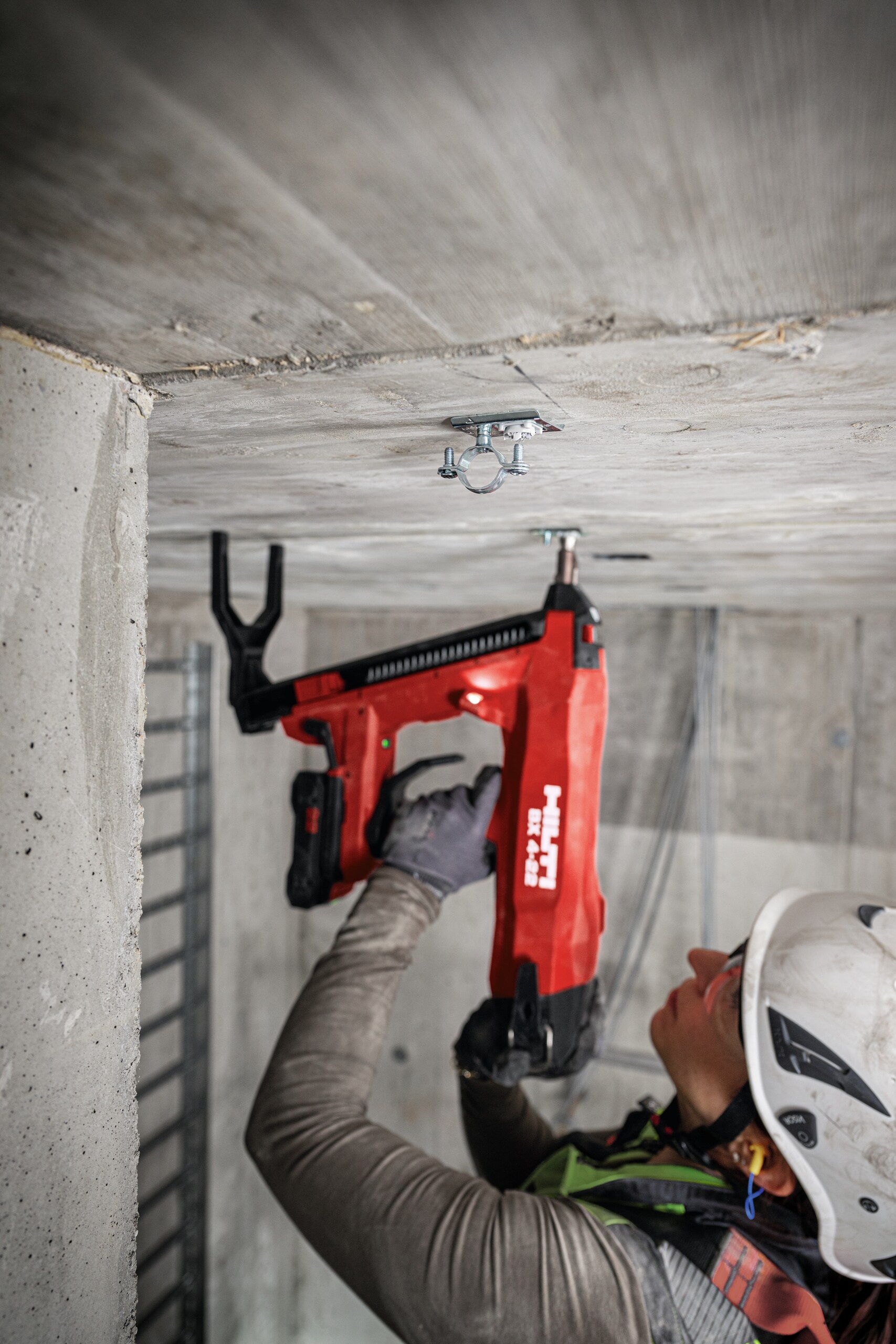 Construction worker doing a roof overhead application using the BX 4-22 with the B22-85 battery to install the BX threaded element with a mounted cable conduit clamp