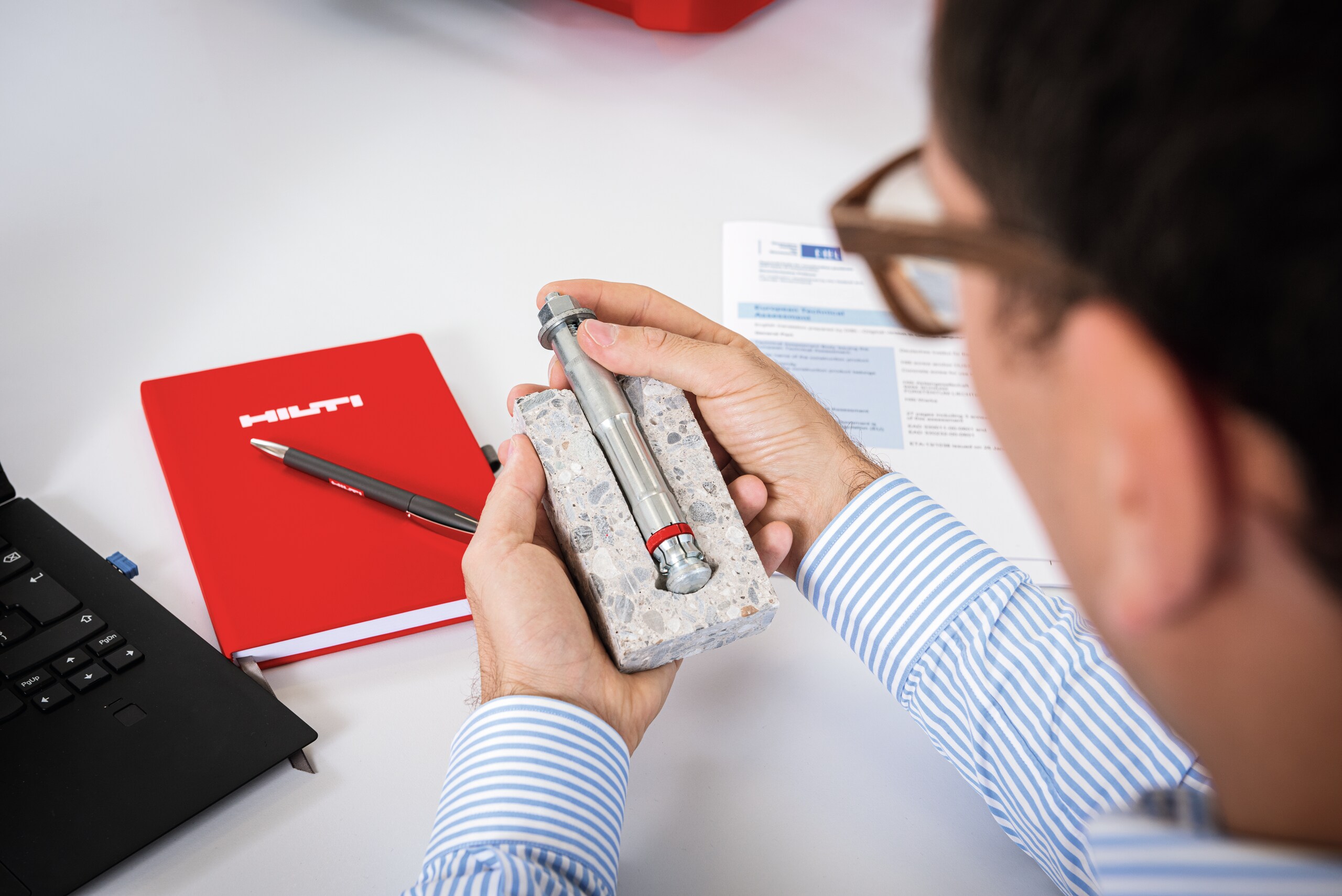 Eine Person untersucht einen Spreizanker, der während einer Engineering-Schulung zu Grundplatten in einem Betonmuster verankert ist.