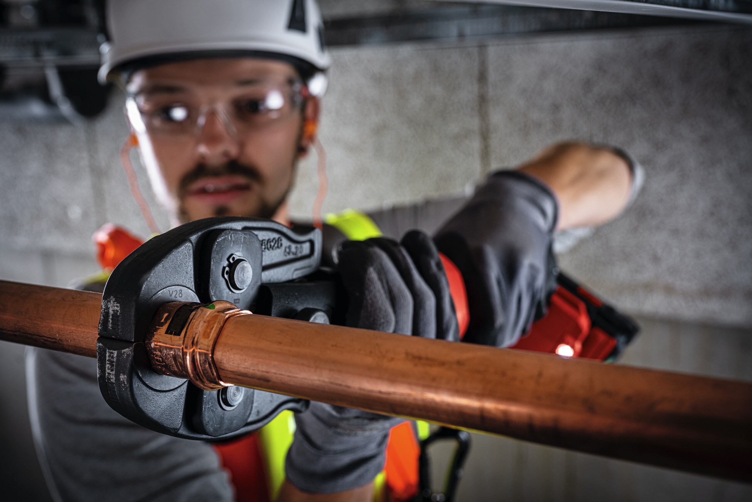 Construction worker using the NPR pipe press tool with hydraulic jaws to connect overhead pipes