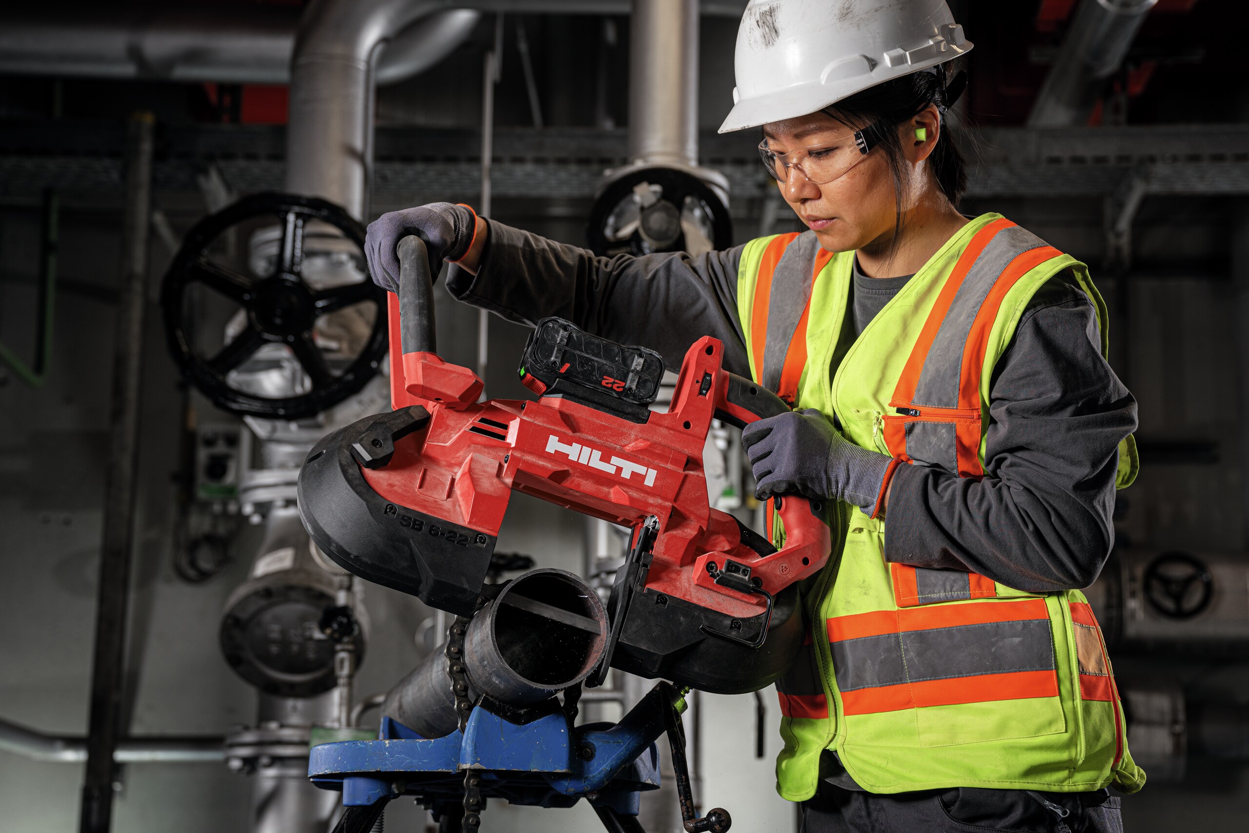 Een werkneemster gebruikt een bandzaag met diepe snede SB 6-22 om een dikke metalen buis te snijden