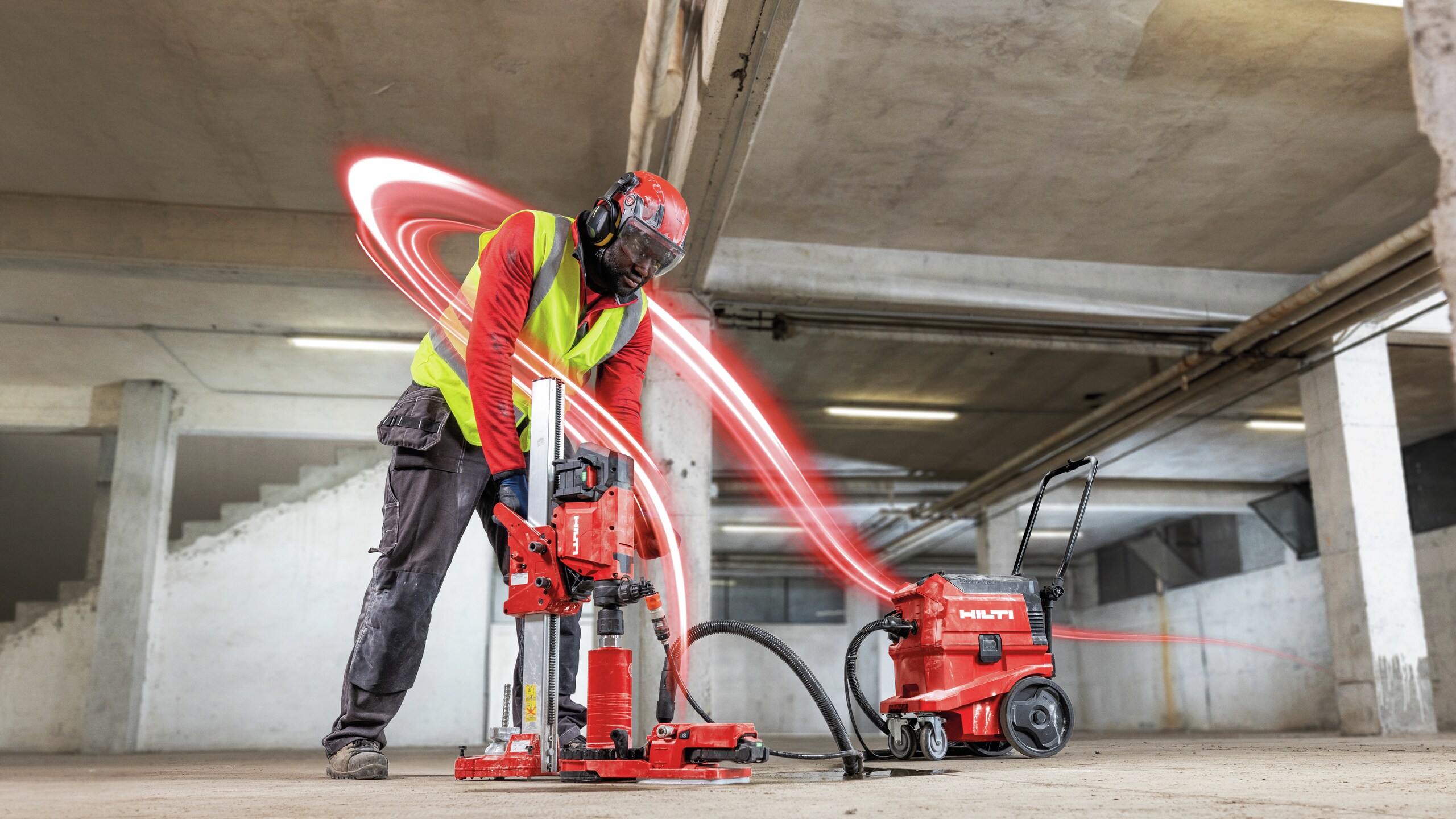 Application image of a worker using a DD 160‑22 Cordless Core Drill with dust extraction to drill a core hole in concrete during indoor construction work.